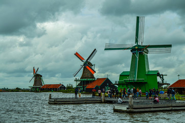 Zaanse Schans, Holland, August 2019. Northeast Amsterdam is a small community located on the Zaan River. View of the mills on the river bank, they stand out with their bright colors. Cloudy day.