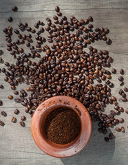 Black coffee ground in a clay mortar and in grains on the surface of a wooden table in sunny rays. Top view.