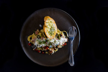Spaghetti with black pepper and bread on black plate. selective focus.