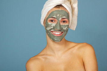 Beautiful cheerful teen girl with dark facial clay mask. Beauty treatments, body care