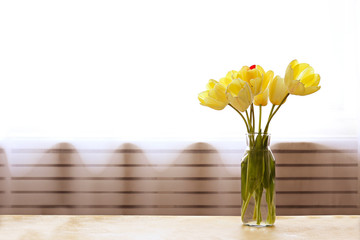 Bouquet of yellow tulip flowers in glass vase on textured table with a lot of copy space for text. Close up.