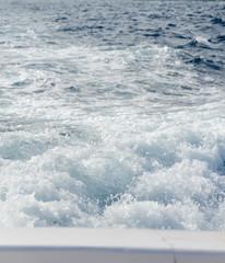 Water splashes and ripples from behind a boat in a blue ocean. boat motion and movement, bubbling splashing water surface. progressive moving forward and leaving behind,