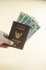 Hand holding Thailand passport with Japanese banknotes