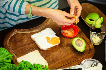 Woman prepares a toast with cheese, salmon and avocado