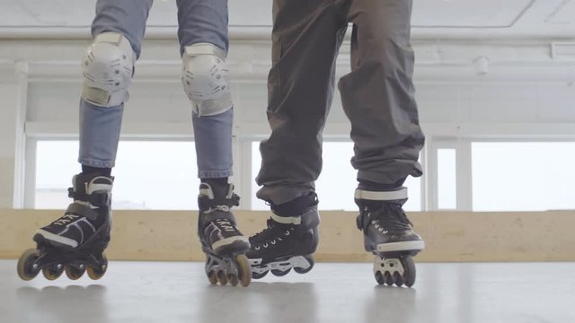 Lockdown of male trainer holding and helping female novice roller-skater wearing protecting gear. She falling down, getting up and continuing training