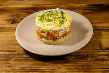 Tasty layered salad with potatoes, chicken breast, marinated mushrooms, carrots, eggs and mayonnaise on wooden table