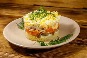 Tasty layered salad with potatoes, chicken breast, marinated mushrooms, carrots, eggs and mayonnaise on wooden table
