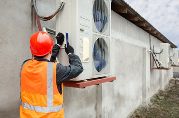 Engineer in protective workwear designing makes notes in his notebook, while standing near the outdoor units of the air conditioner or heat pump