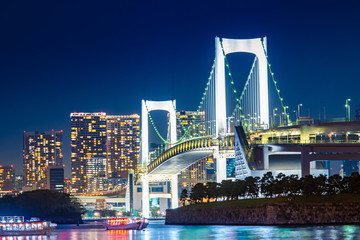 Japan. View of Tokyo at night from the island of Odaiba. Illumination of the Rainbow Bridge. Lights of the night city in Japan. Bridge in the night bay. Excursion ferries in Tokyo. Japan bridge.