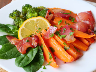 Baked sweet potato wedges with fried bacon bits, baby spinach, broccoli and lemon on plate