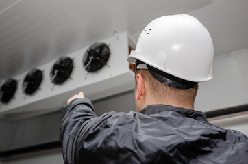 The repairman in overalls and a protective helmet carries out diagnostics of the warehouse air conditioning system. professional repair of the ventilation system