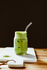 Matcha green tea latte in a glass jar with glass tube on a white marble tray. Healthy clean eating concept.