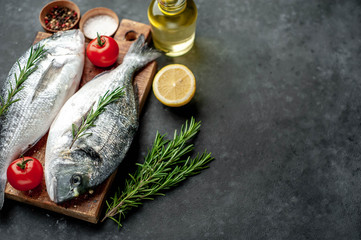 Fresh dorado fish with spices and ingredients tomato, razmorin, sunflower oil, lemon for cooking on a stone background with copy space for your text