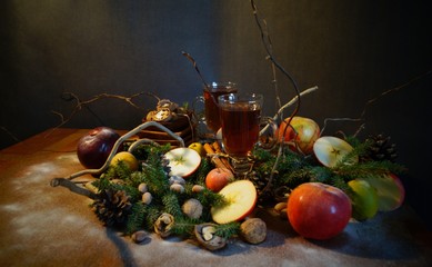 tea in glass mugs in the cold season among sticks of cinnamon, nuts, quince, apples and spruce branches on a wooden table on a black background