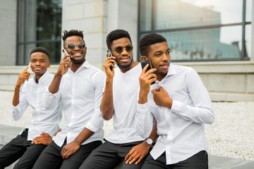 Obraz premium four handsome young african men in white shirts with phones in their hands