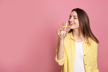 Young woman drinking lemon water on pink background. Space for text