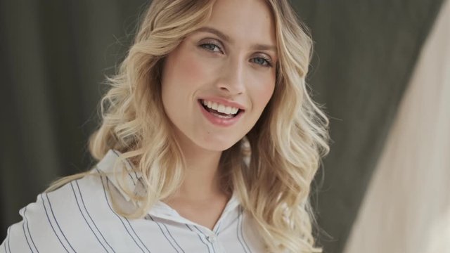 A flirty blonde woman is looking to the camera and smiling isolated over fabric background