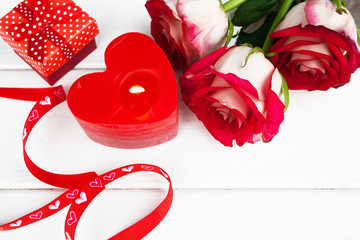 Beautiful red roses and romantic candle by the day of the valentine on a white wooden background