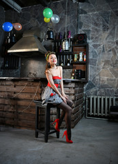 beautiful pin-up girl in a gray-red dress sitting on a bar stool and posing