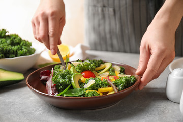 Woman cooking tasty kale salad on light grey table, closeup