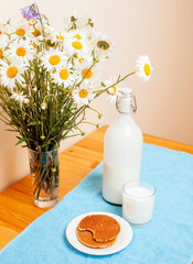 Simply stylish wooden kitchen with bottle of milk and glass on table, summer flowers camomile, healthy foog moring concept close up