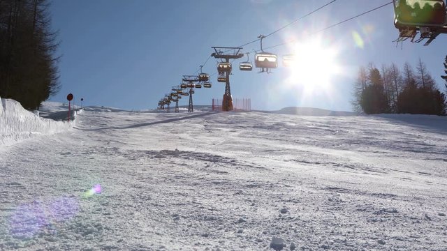 Chairlift lifts skiers up the mountain above an empty ski slope in the rays of the sun. Livigno, Italy