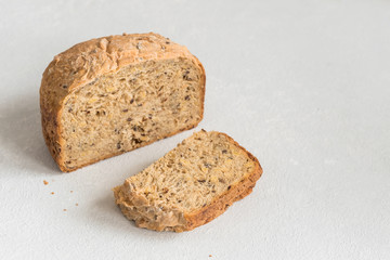 Half a loaf of homemade whole grain bread with various seeds and two slices on a white background. Healthy natural fresh food. Close-up