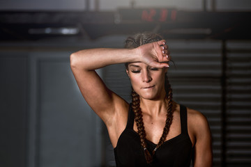 Young sweaty beautiful muscular fit girl sweep sweat from her forehead with her hand after heavy hardcore crossfit workout training in the gym - obrazy, fototapety, plakaty