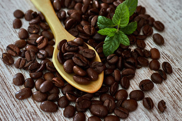 Wooden teaspoon between coffee beans, and mint leaves