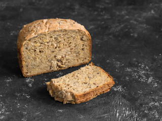 Half a loaf of homemade whole grain bread with various seeds and two slices on a black background. Healthy natural fresh food. Close-up