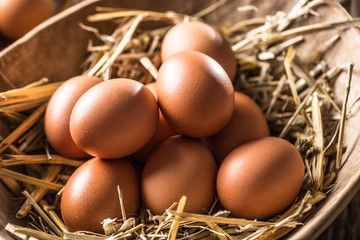 Fresh raw eggs in straw and wooden bowl on rustic wooden table