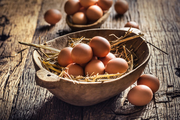 Fresh raw eggs in straw and wooden bowl on rustic wooden table