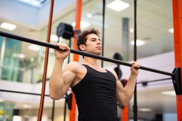 Man doing free body calisthenic pull-ups in a gym