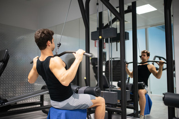 Fototapeta na wymiar Man using a lat machine in a gym to train his shoulders and back
