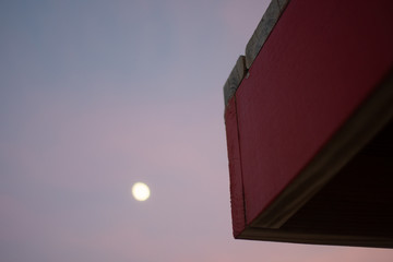 Fototapeta na wymiar the corner of a life guard stand takes up the frame camera right as the moon shines high at sunset in the distance 