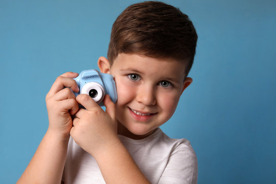 Little photographer with toy camera on light blue background