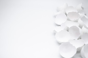 Lots of broken white eggshells on a white background. On the left. Copy space