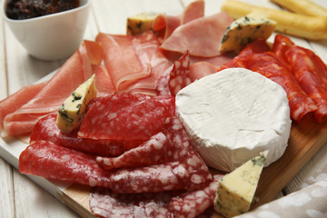 Tasty ham with other delicacies served on white wooden table, closeup