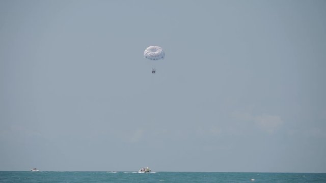 People fly by parachute over the open sea, towed by a motor boat. Tourists enjoy the beauty of the landscape.