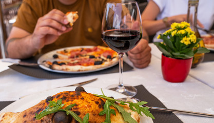 Baked traditional italian pizza on the plate. Man eating pizza at restaurant. Man's hands taking of fresh pizza with tomatoes and olives.