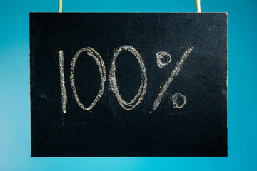 Chalk board is hanging with the inscription "100%" on a blue background. copy space