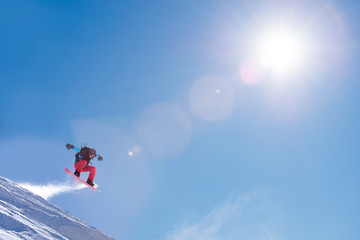 Fototapeta na wymiar Snowboarder Jumping High on Snowboard in Mountains at Sunny Day. Snowboarding and Winter Sports