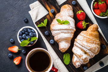 Croissant with fresh berries and cup of coffee on black.