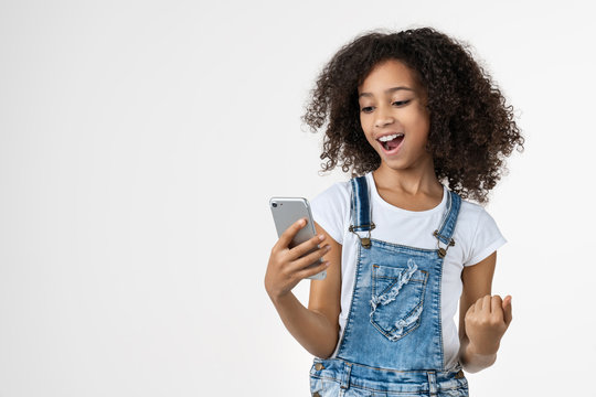 Happy Young African Girl Kid Using Mobile Phone Make Winner Gesture Posing Isolated Over White Background
