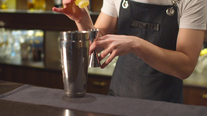 Bartender pours different syrups in shot glass and shaker 