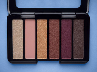 Nude eyeshadow palette in black case top view isolated on blue background. Neutral .beige, pink,...