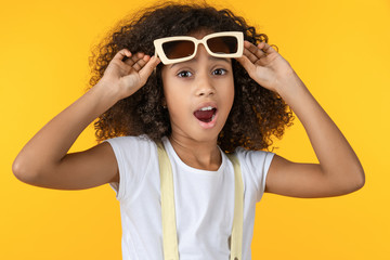 Close up of young girl wearing sunglasses excited isolated on yellow background