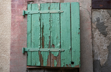 Green wooden window shutters of a old mediterranean house with vintage wall plaster. Green weathering and destruction shutters on old building.