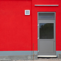Detail of a red wall with a door, fluorescent tube and a fan