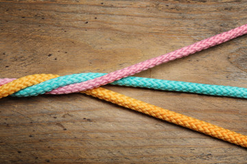 Twisted colorful ropes on wooden background, top view. Unity concept